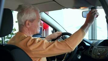 Senior man adjusts rearview mirror inside the car video