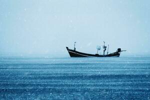 Fishing boat on the sea with snowfall in winter color tone. photo