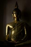 un estatua de oro Buda con sombra en pared en el oscuro habitación foto