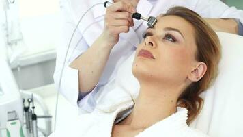 Cosmetologist moves iontophoresis roller along client's forehead video