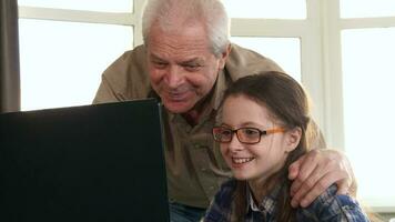 pequeño niña y su abuelo tener vídeo charla en ordenador portátil video