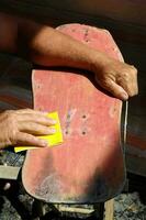 un hombre es lijado un patineta con un amarillo esponja foto