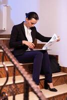 Overworked tired businesswoman reading financial raport of deadline project in the evening. Serious entrepreneur working on job project sitting on staircase of business building at night hours for job. photo