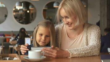 mor och dotter använda sig av smartphone på de Kafé video
