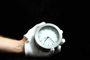 a person in white gloves holding a clock photo