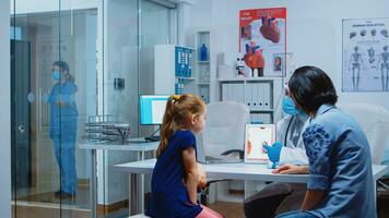 Doctor explining to child the functions of heart using tablet and wearing facial protection. Pediatrician specialist with gloves providing health care services consultations treatment during covid19 photo