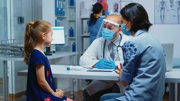 Close up of girl portrait talking with doctor about her symptoms. Pediatrician specialist in medicine with mask providing health care service consultation treatment in hospital cabinet during covid19 photo