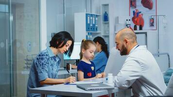 Mother completing a medical questionnaire with daughter data in medical office. Specialist in medicine providing health care services consultation diagnostic examination treatment in hospital cabinet photo