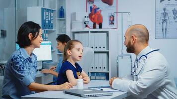 Child and doctor talking in clinic while nurse checking pills. Pediatrician specialist in medicine providing health care services consultation diagnostic examination treatment in hospital cabinet photo