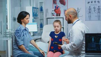 Male doctor writing child diagnostic on tablet talking with woman. Healthcare practitioner physician specialist in medicine providing health care services consultation treatment in hospital photo