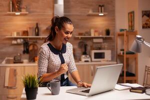 Portrait of happy businesswoman with clenched fist after finishing a deadline working from home. Employee using modern technology at midnight doing overtime for job, career, network, lifestyle. photo