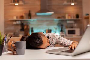 Woman falling asleep with head on the table while working from home on a deadline. Employee using modern technology at midnight doing overtime for job, business, career, network, lifestyle ,wireless. photo