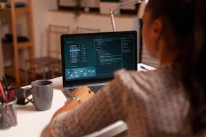 Female hacker sitting in front of computer and thinking how to fraud the government at night time. Programmer writing a dangerous malware for cyber attacks using performance laptop during midnight. photo