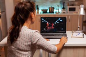 dama jugando juegos en ordenador portátil durante noche hora durante noche hora en hogar cocina. profesional jugador jugando en línea videop juegos en su personal computadora. friki ciber deporte foto