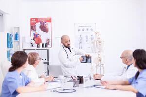 Young doctor giving presentation to colleagues in conference room holding xray. Clinic expert therapist talking with colleagues about disease, medicine professional. photo