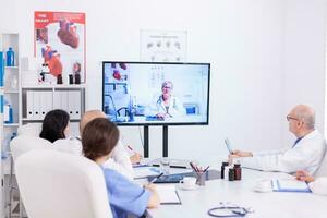 Team of medical staff during video conference with doctor in hospital meeting room. Medicine staff using internet during online meeting with expert doctor for expertise. photo