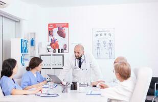 Young medical specialist discussing about patient diagnosis with coworkers in hospital conference room. Clinic expert therapist talking with colleagues about disease, medicine professional photo