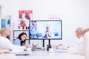 grupo de doctores que se discute con experto durante vídeo conferencia desde hospital reunión habitación. medicina personal utilizando Internet durante en línea reunión con experto médico para pericia. foto