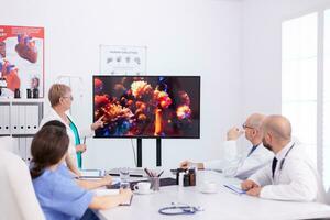 Mature expert doctor talking about global pandemic with coronavirus in conference room for colleagues. Virolog specialist doctor discussing with colleagues about global pandemic because of dangerous virus, symptoms. photo