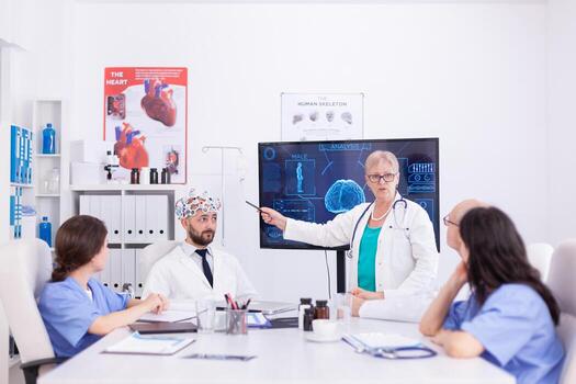 Scientist doing brain analysis using headset with sensors on doctor in hospital meeting room. Monitor shows modern brain study while team of scientist adjusts the device. photo