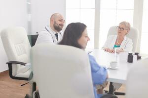 Medical staff smiling in meeting room while talking with other medical practitioner wearing white coat. Clinic therapist with colleagues talking about disease, expert,specialist, communication. photo