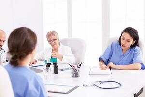 Doctors having a medical discussion with her staff during team meeting. Clinic expert therapist talking with colleagues about disease, medicine professional. photo