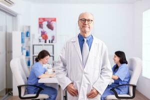 Elderly aged expert doctor in hospital conference room wearing lab coat. photo