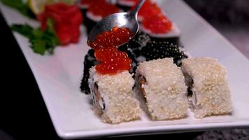 Sticks Take Sushi in restaurant lights background. Variety of types sushi with red caviar, fish, Philadelphia cheese and chopsticks closeup. Set of delicious Japanese sushi rolls on a stone board video