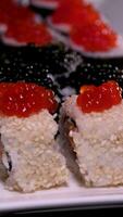 Gravetos levar Sushi dentro restaurante luzes fundo. variedade do tipos Sushi com vermelho caviar, peixe, Filadélfia queijo e pauzinhos fechar-se. conjunto do delicioso japonês Sushi rolos em uma pedra borda video