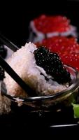 Gravetos levar Sushi dentro restaurante luzes fundo. variedade do tipos Sushi com vermelho caviar, peixe, Filadélfia queijo e pauzinhos fechar-se. conjunto do delicioso japonês Sushi rolos em uma pedra borda video