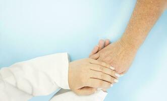 The hands of a doctor hold the hands of an old woman on a blue background. photo