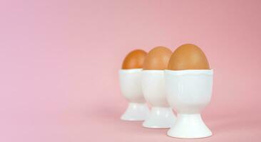 Eggs in egg cups on a pink background. Easter composition with copy space. photo