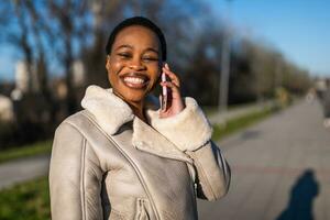 Outdoor portrait of happy black woman. She is talking on phone. photo