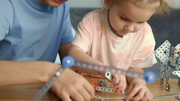 niños jugar con un metal constructor a el mesa a hogar.madres día, familia juegos, hogar educación,educativo juegos video