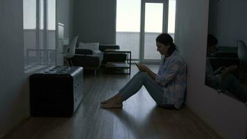 A woman cries after reading a message on a smartphone while sitting on the floor at home. video