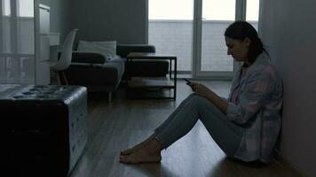 A woman cries after reading a message on a smartphone while sitting on the floor at home. video