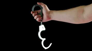 bare caucasian hand holding opened silver steel handcuffs on black background video