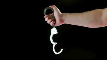bare caucasian hand holding opened silver steel handcuffs on black background video