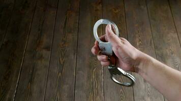 bare caucasian hand holding silver steel handcuffs on wooden board background video