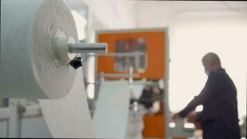 An elderly man in a medical mask works in a factory near the conveyor for the manufacture of respiratory protective equipment. Coronovirus and Covid-19 Prevention video