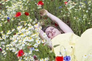 a beautiful young blonde woman in a yellow dress stands among a flowering field photo