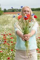 hermosa de edad mediana rubia mujer soportes entre un floración campo de amapolas foto