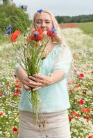 beautiful middle-aged blonde woman stands among a flowering field of poppies photo