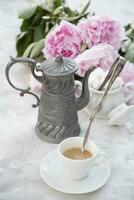 vintage still life with a cup of coffee against a bouquet of pink peonies photo