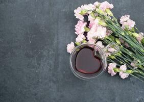 rosado claveles en un oscuro antecedentes con un taza de rojo té en un en forma de corazon taza foto