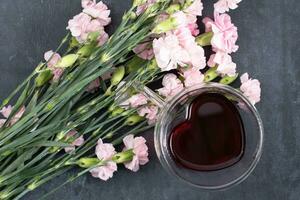 rosado claveles en un oscuro antecedentes con un taza de rojo té en un en forma de corazon taza foto