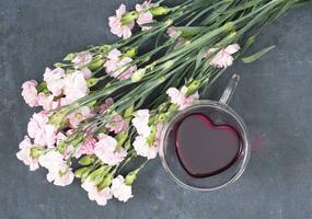 rosado claveles en un oscuro antecedentes con un taza de rojo té en un en forma de corazon taza foto