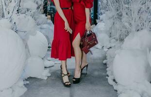 de cerca ver de dos De las mujeres piernas en alto tacones en pie vistiendo un rojo vestir en un piso decorado con nieve. Días festivos y celebracion concepto. foto