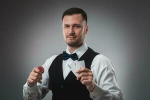 Young man in shirt and waistcoat shows his cards and holds poker chips in his hands, studio shot photo