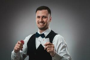 Young man in shirt and waistcoat shows his cards and holds poker chips in his hands, studio shot photo